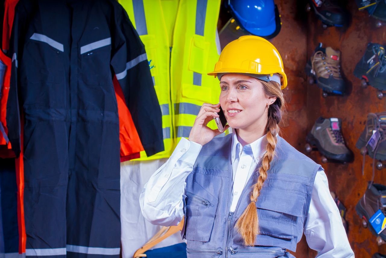 hero-img-01 Woman engineer in safety gear with braided hair talks on phone in industrial setting.
